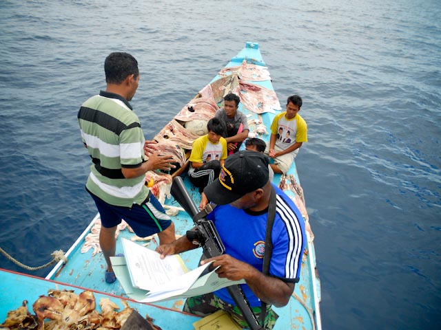 ci_54200860 A Raja Ampat police officer reviews a fishing vessel's documents.